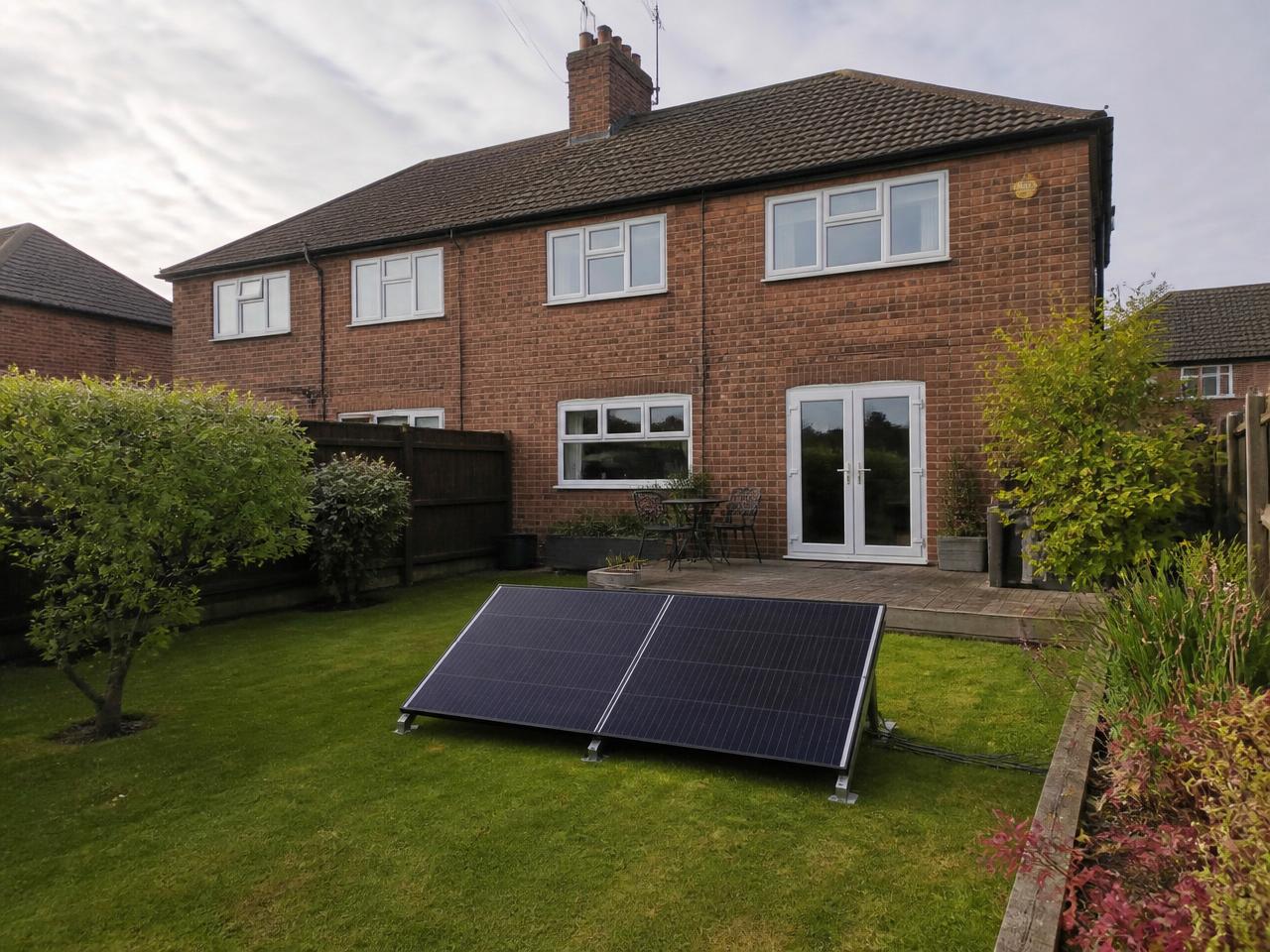 A modest UK brick house with a compact two-panel ground-mounted solar kit on the lawn